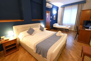 A hotel room with a large bed, bedside tables, a desk, a chair, and a television.