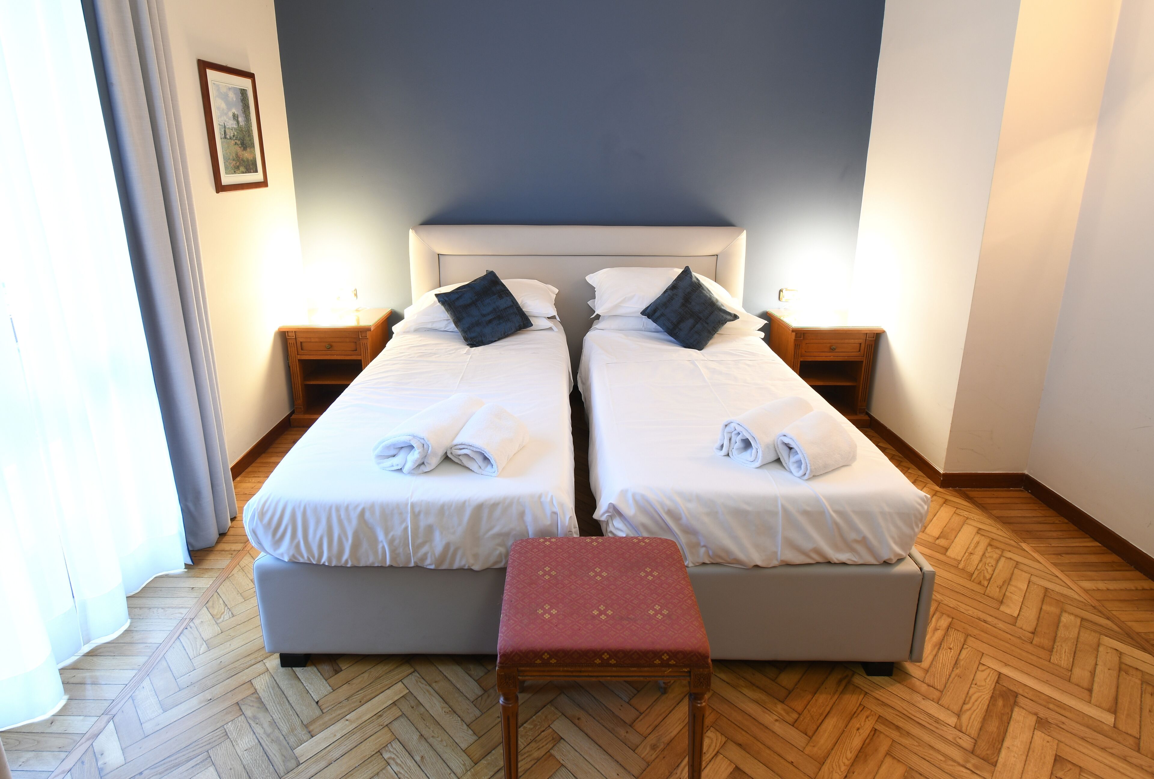 Ein Doppelbett mit weißer Bettwäsche und dunklen Kissen, eine Holzbank und ein Nachttisch mit einer Lampe.