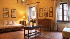 A cozy room with a wooden bed, a wooden table with a vase of flowers, and a wooden dresser. There are framed pictures on the walls and a window with curtains. - Castello Di Petroia Relais (Gubbio)