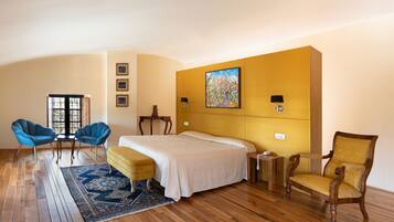 Camera d'albergo con un letto grande, due poltrone, un pavimento in legno e un quadro appeso al muro.