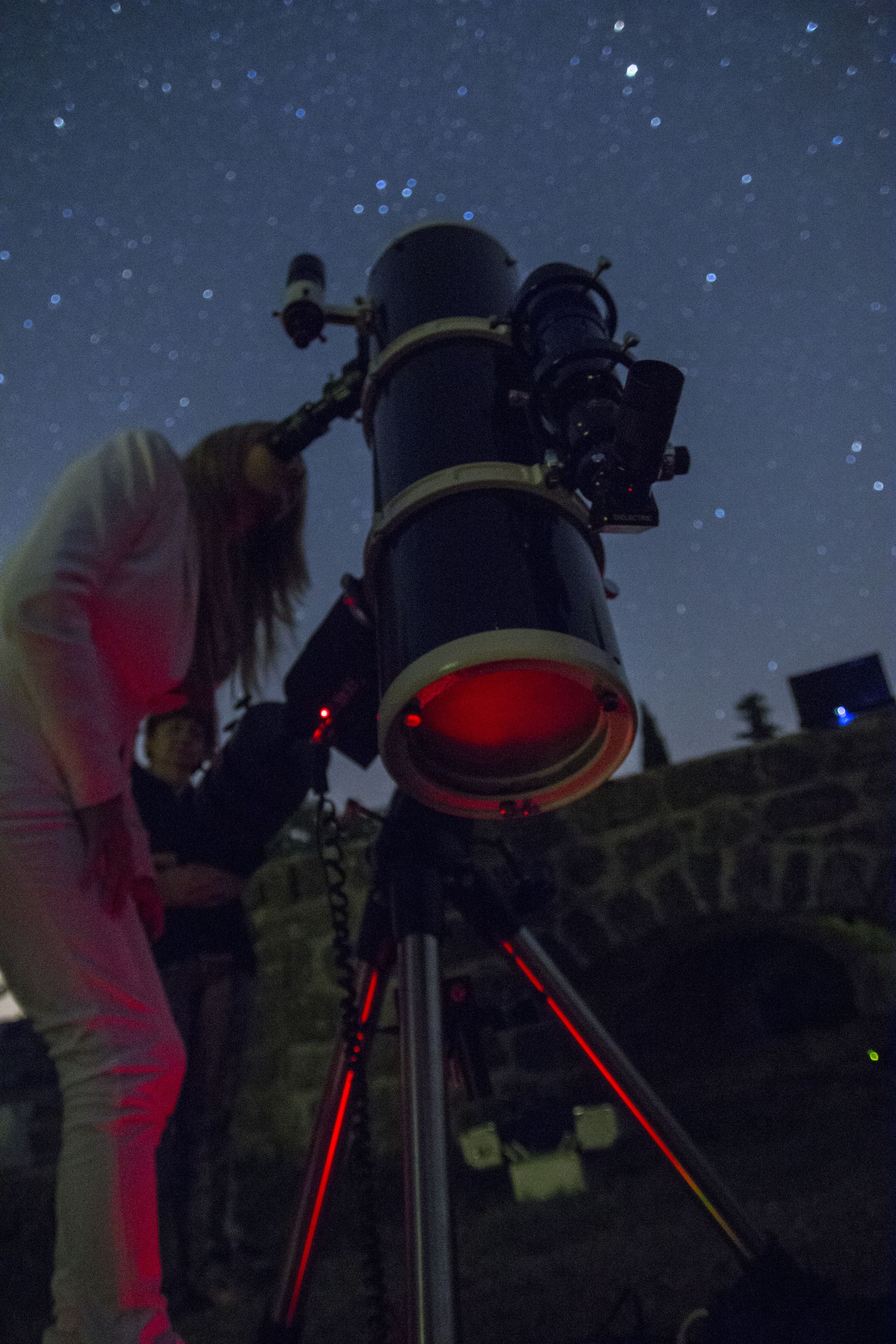 A telescope with a red light, set against a night sky with stars.