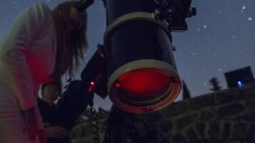 A telescope with a red light, set against a night sky with stars.