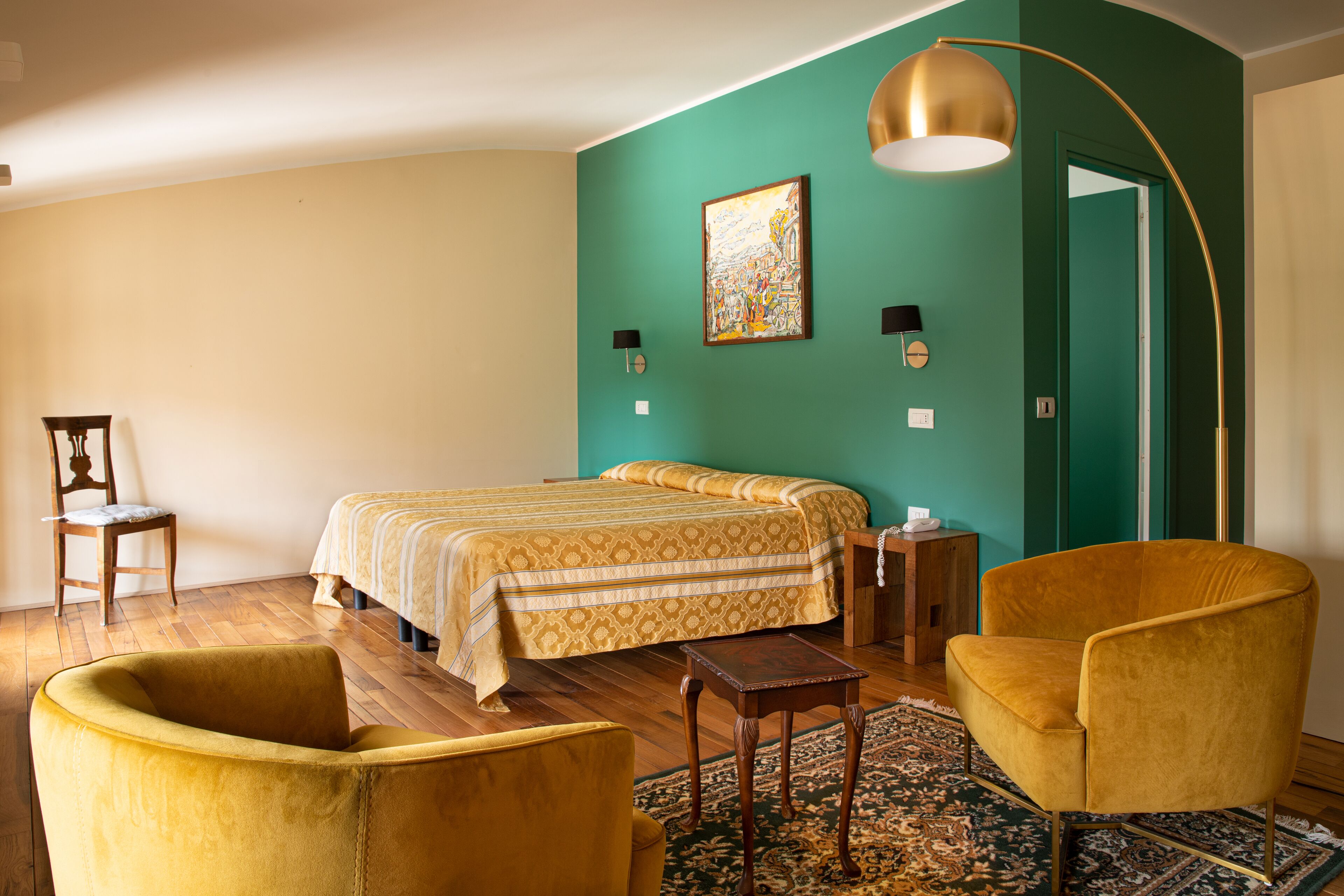 Quarto com cama, duas cadeiras, mesa de cabeceira, luminária e pintura na parede.