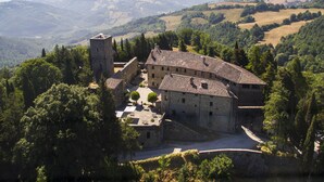 A historic stone building with a courtyard, surrounded by trees and hills. - Castello Di Petroia Relais (Gubbio)