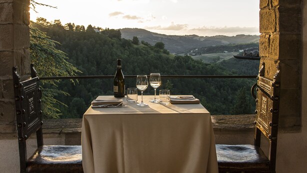 A table set for two with a bottle of wine and glasses, overlooking a scenic landscape with hills and trees. - Castello Di Petroia Relais (Gubbio)