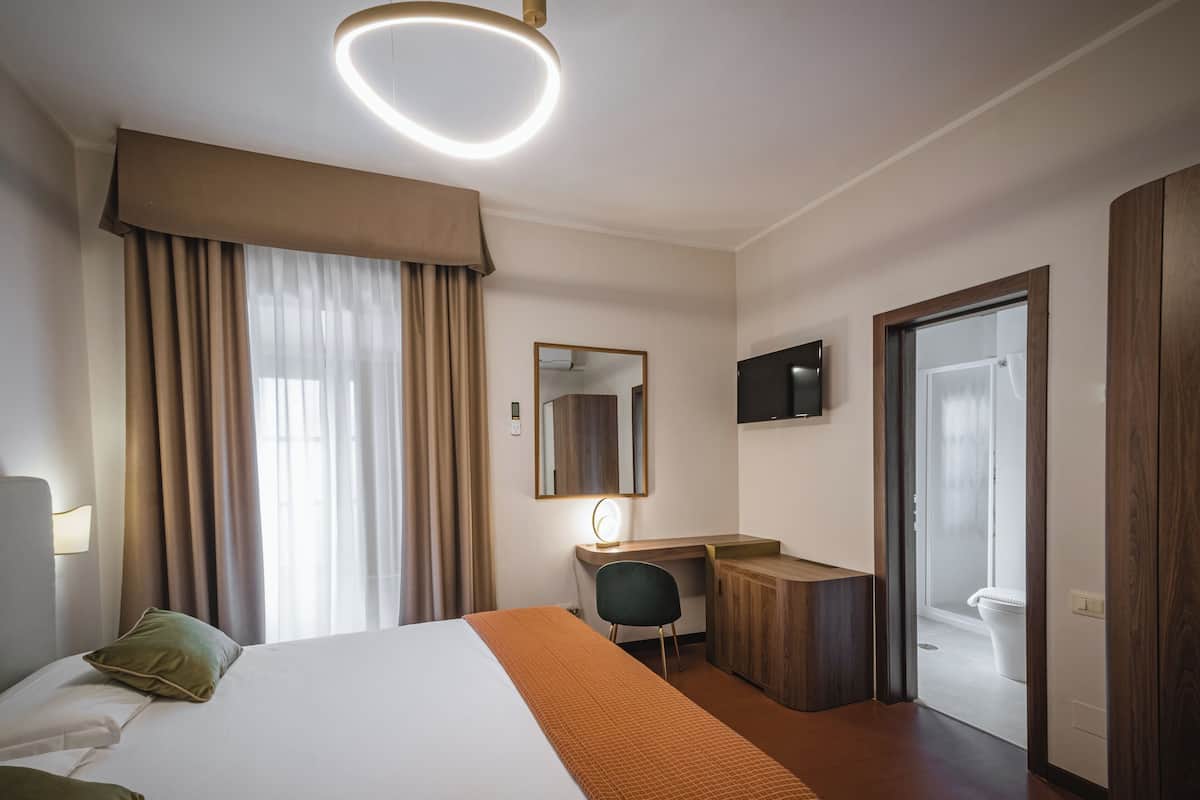A hotel room with a bed, desk, chair, and a television.