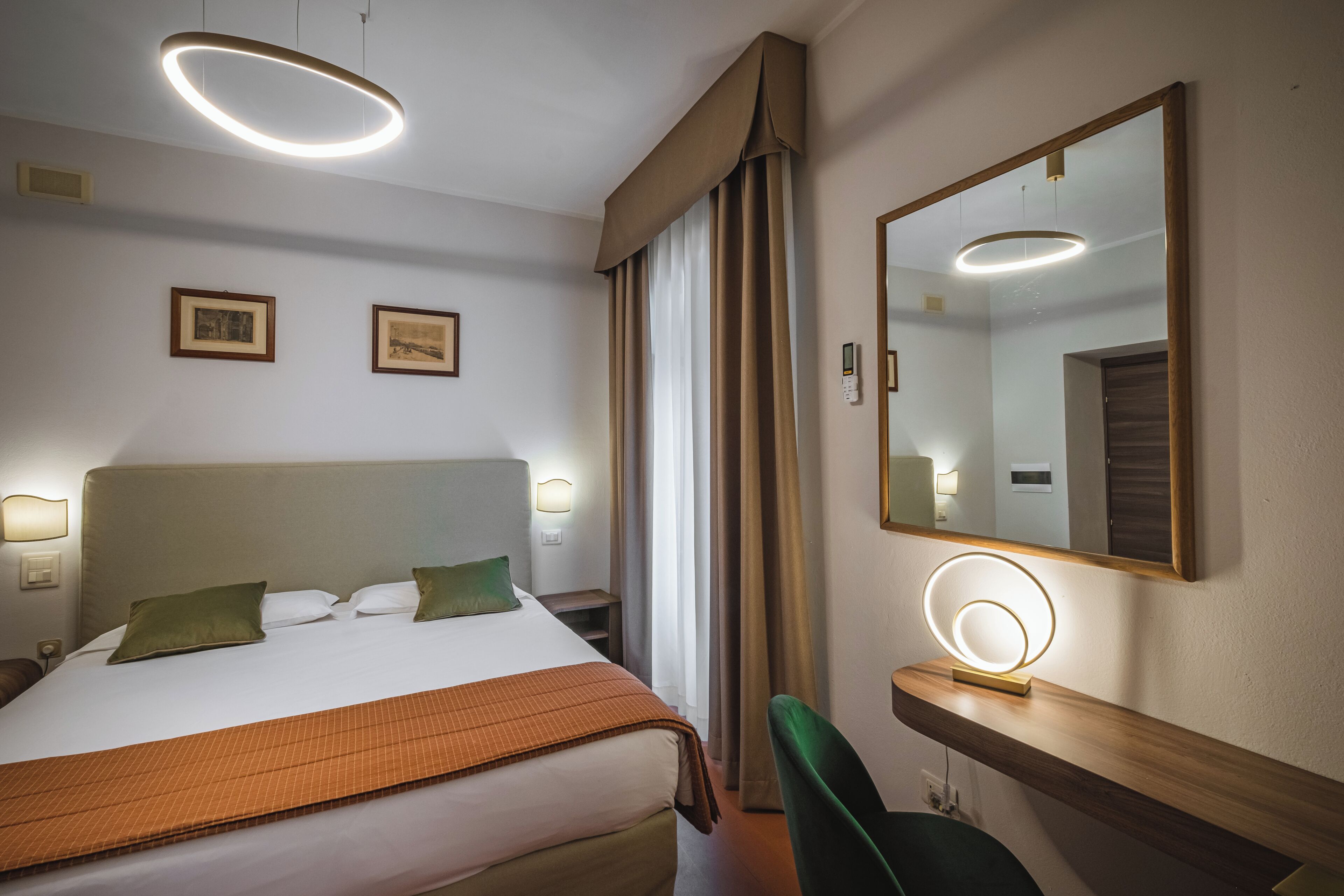 Una habitación de hotel con una cama grande, lámparas de noche, un espejo y un escritorio con un aro de luz.