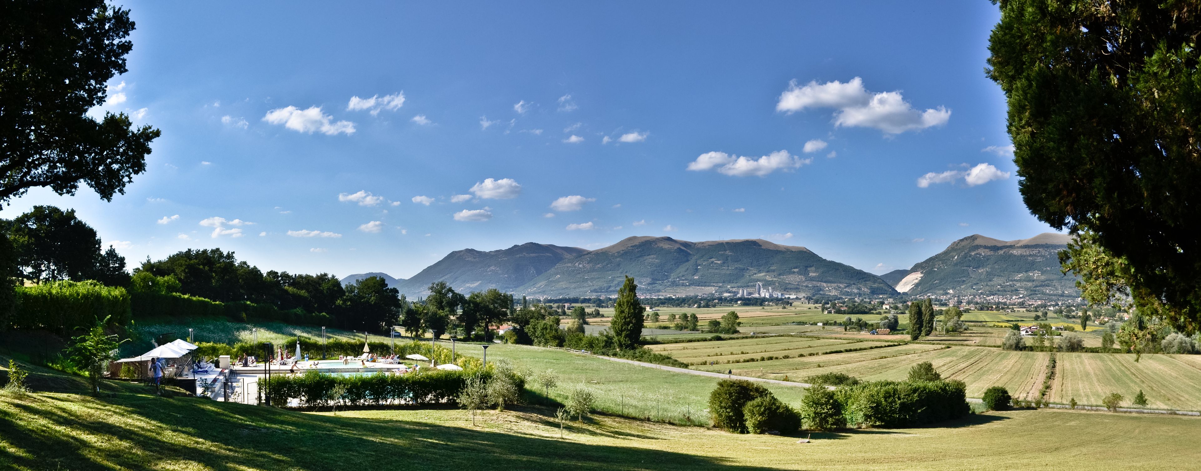 Paisaje rural con campos, piscina y montañas al fondo.