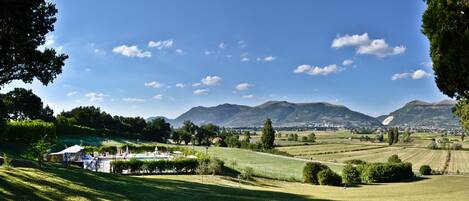 Paisaje rural con campos, piscina y montañas al fondo.