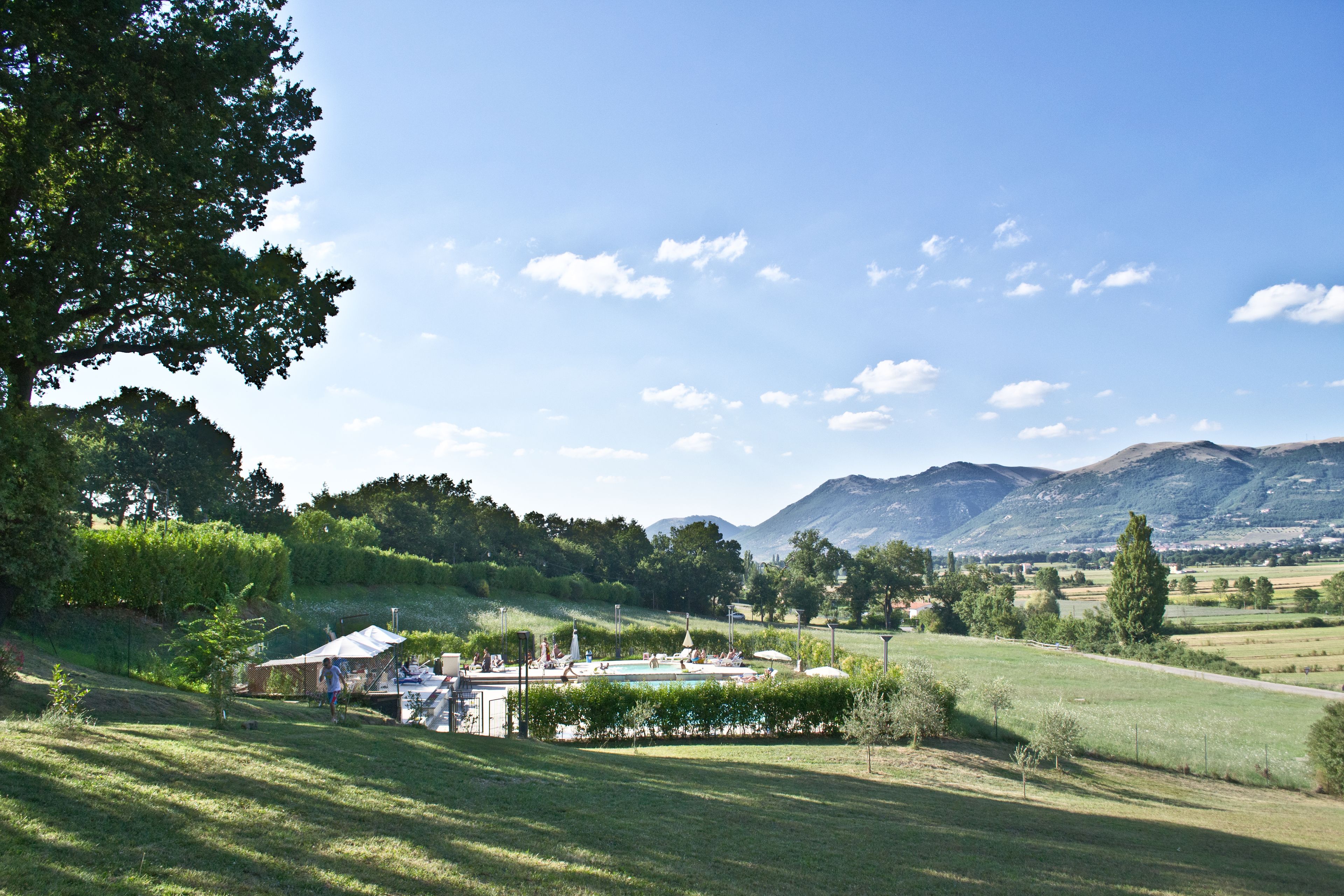 A rural landscape with a swimming pool, tents, and a clear view of mountains in the background.