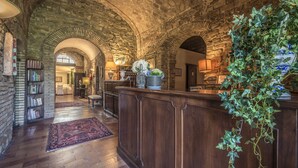 A spacious lobby with a high ceiling, stone arches, a wooden reception desk, and a large potted plant. - Hotel Villa Montegranelli (Gubbio)