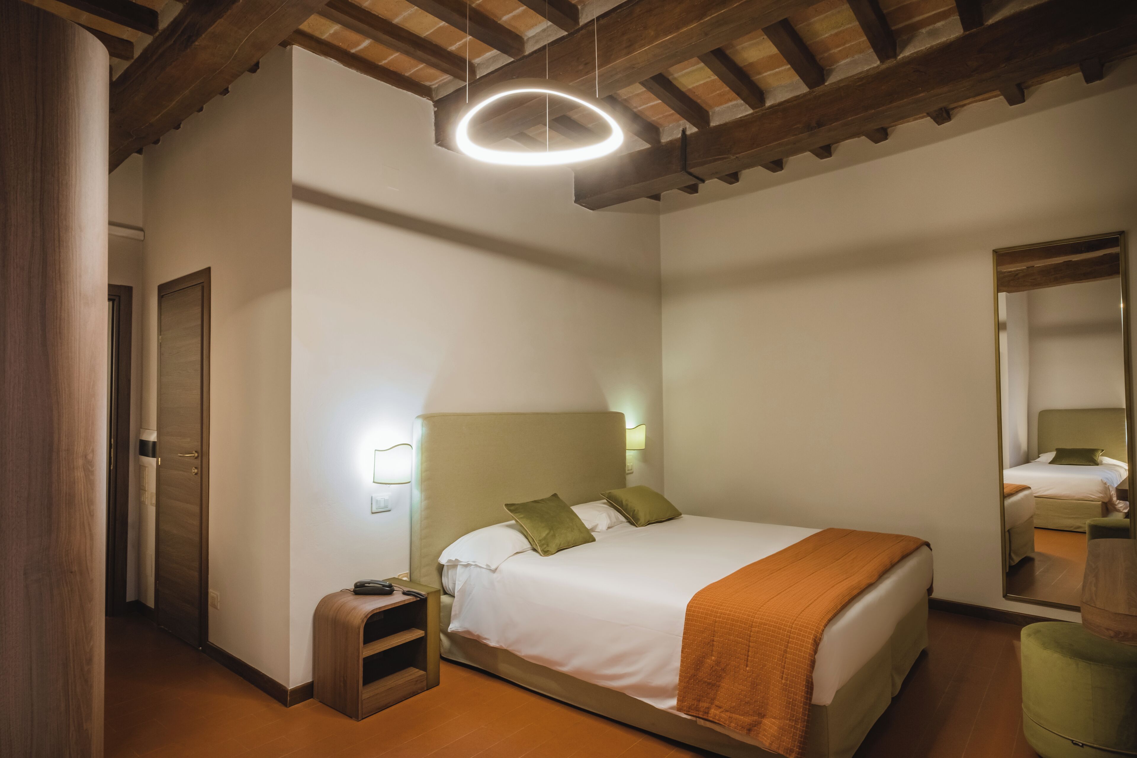 A bedroom with a bed, bedside table, nightstand, and a mirror.
