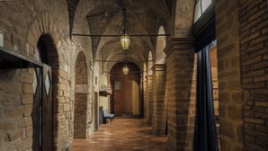 A corridor with stone walls, wooden doors, and a checkered floor. - Hotel Villa Montegranelli (Gubbio)