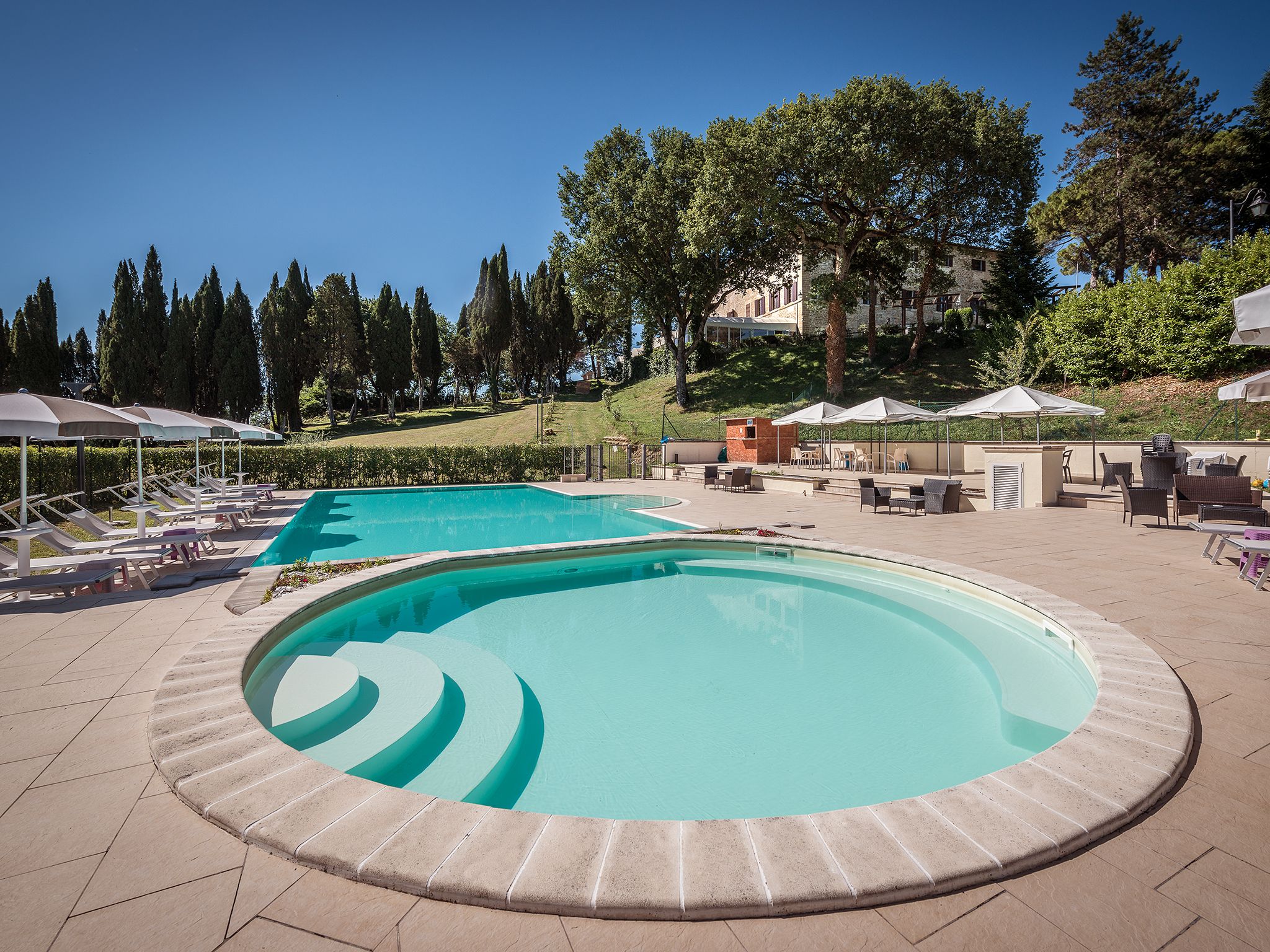 A pool area with two pools, lounge chairs, and umbrellas.