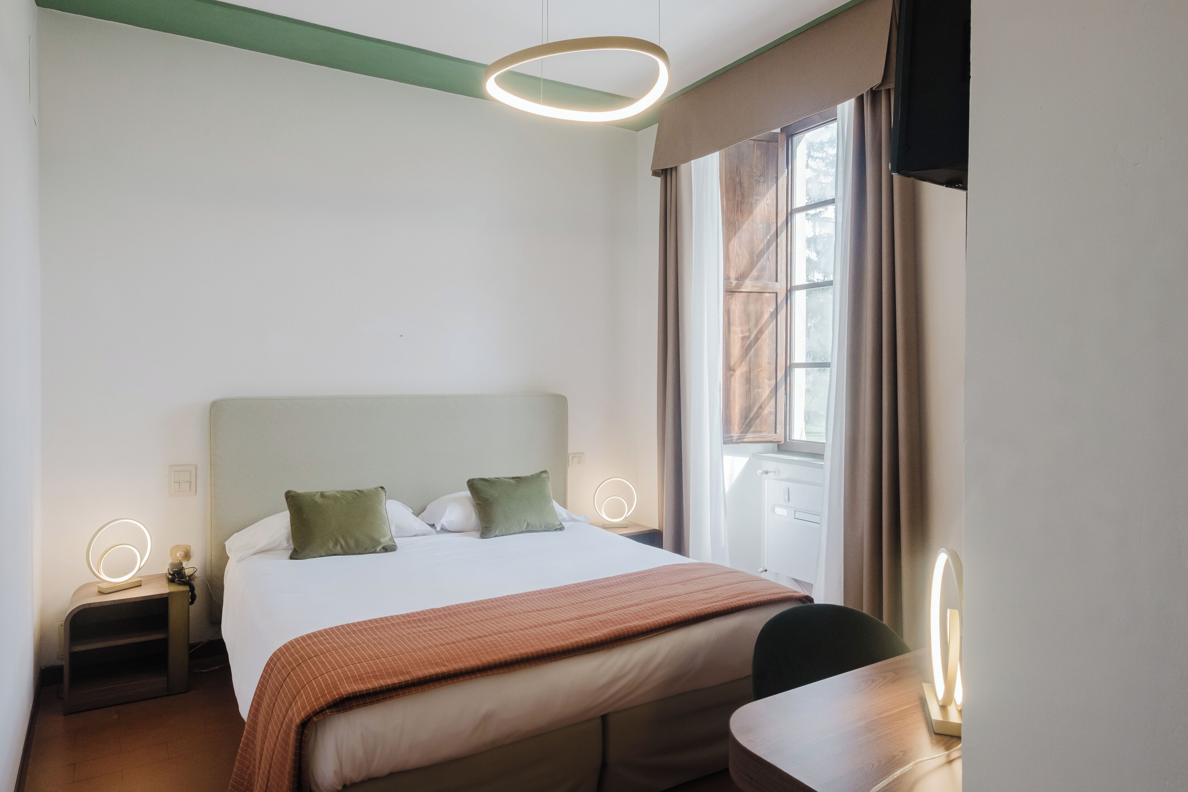 Une chambre d’hôtel avec un lit, des tables de chevet, un bureau et une fenêtre avec des rideaux.