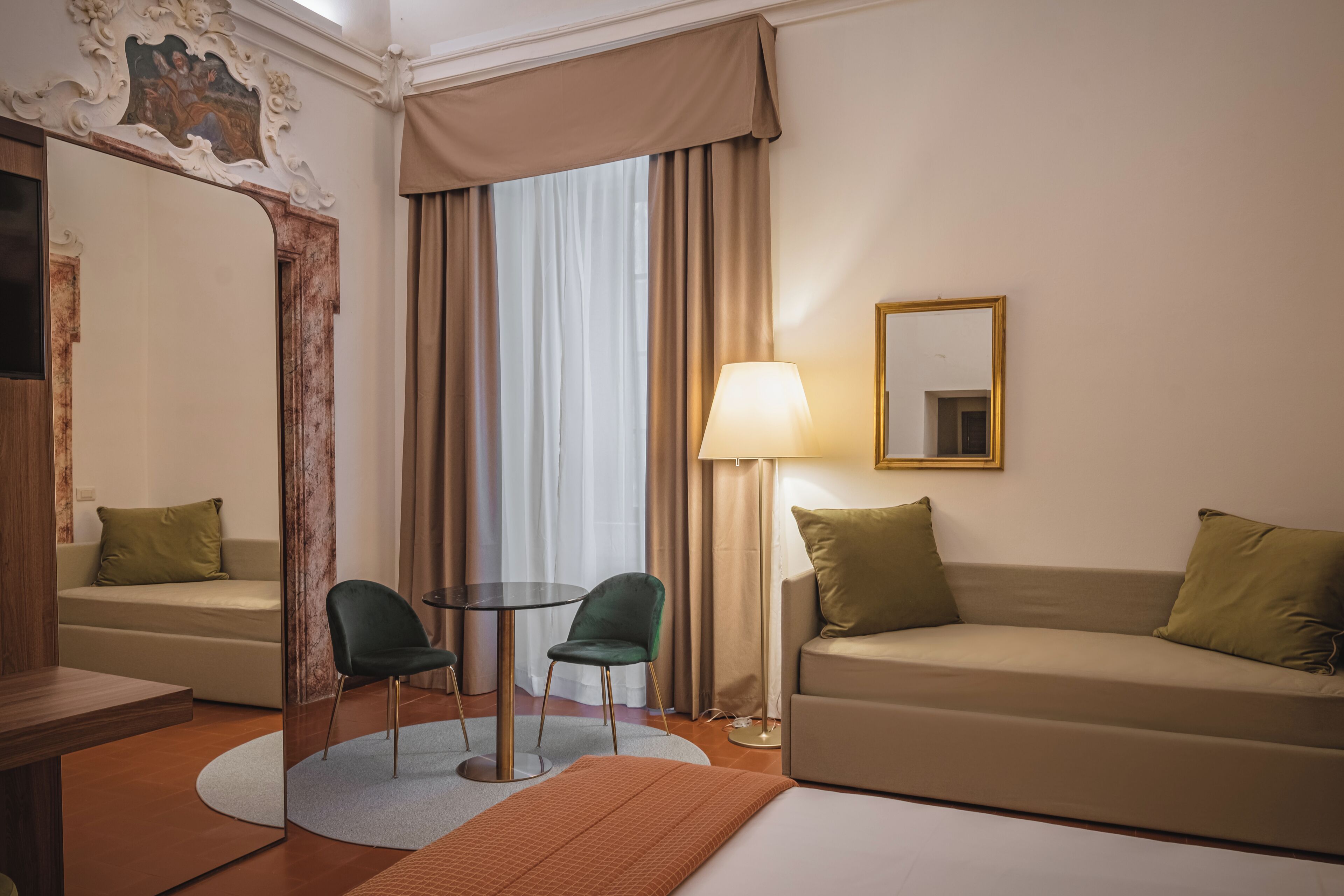 Une chambre d’hôtel avec un canapé, deux fauteuils, une table, une lampe et un miroir.