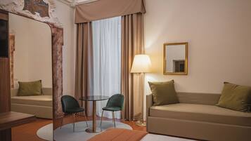 Une chambre d’hôtel avec un canapé, deux fauteuils, une table, une lampe et un miroir.
