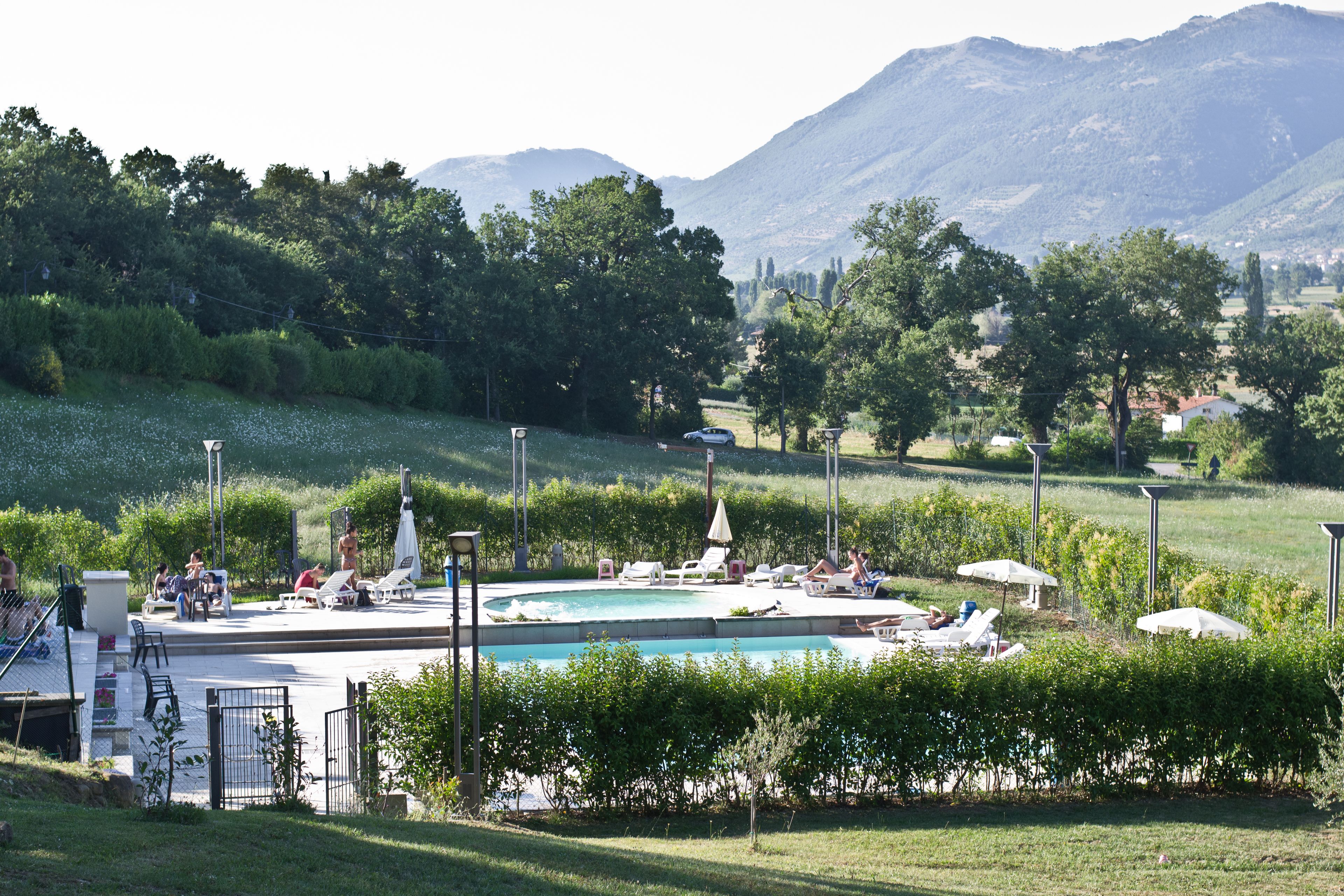 Un espace piscine doté de chaises longues et de parasols, entouré de verdure et avec des montagnes en toile de fond.
