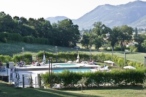 A pool area with lounge chairs and umbrellas, surrounded by greenery and mountains in the background. - Hotel Villa Montegranelli (Gubbio)
