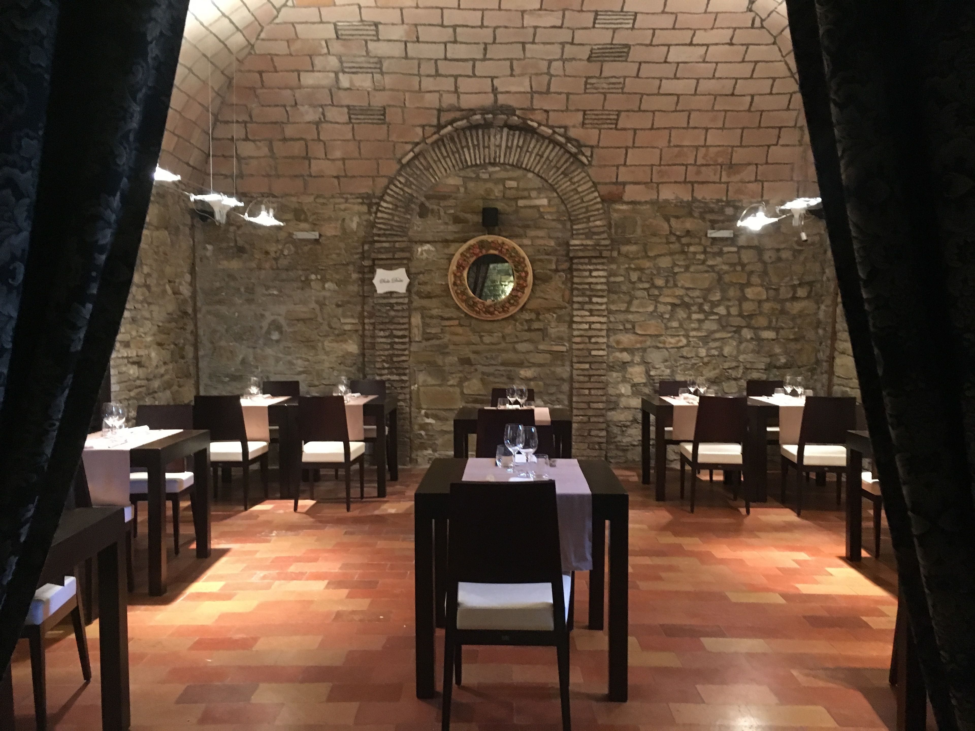 A restaurant with a stone wall and arched ceiling, featuring tables and chairs set for dining.