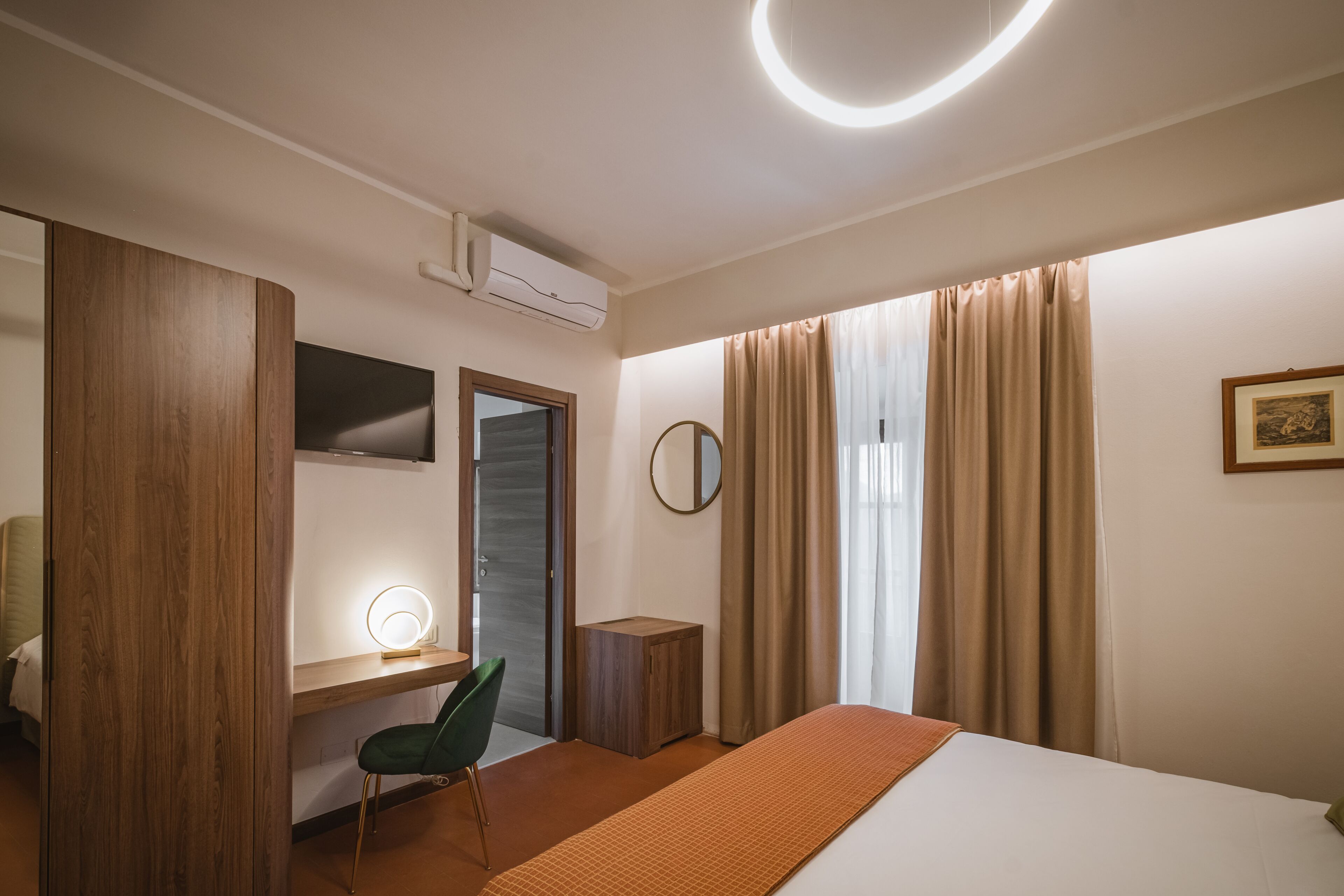 Una habitación de hotel moderna con una cama, un escritorio con silla, un espejo y una mesita de noche.