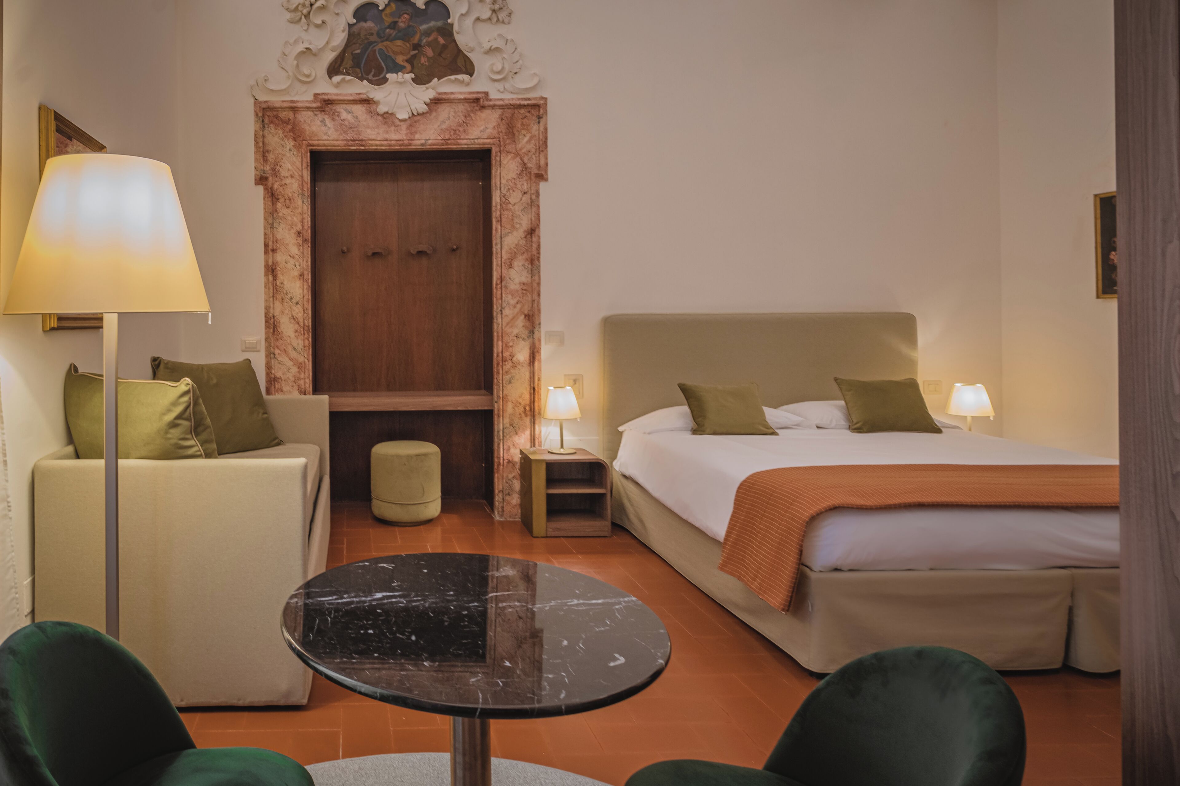 A hotel room with a bed, a sofa, a table, and a lamp.