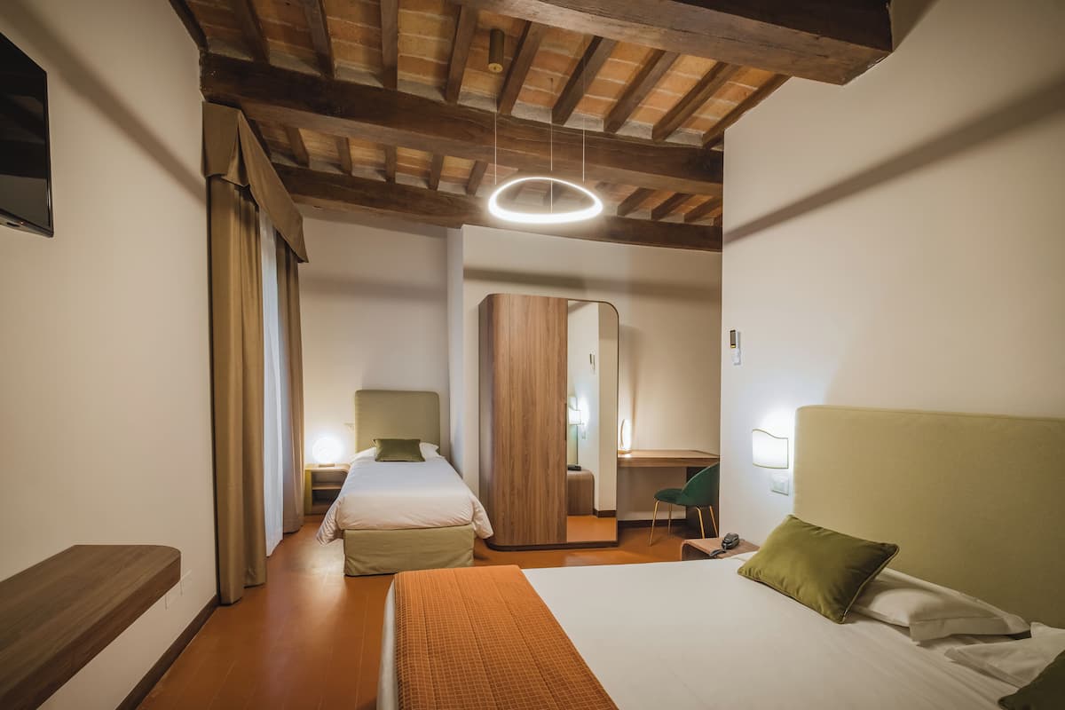 A hotel room with a wooden ceiling, a bed with a green pillow, a desk with a chair, and a mirror.