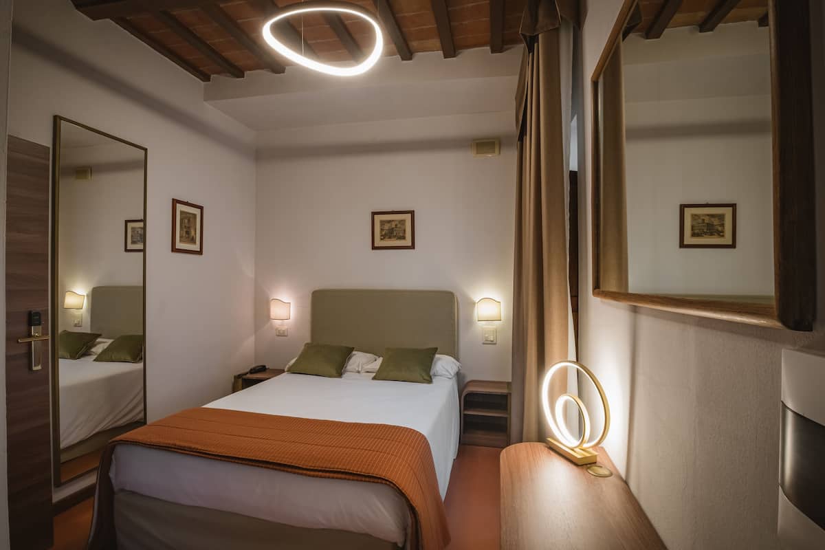 A hotel room with a large bed, bedside lamps, a mirror, and a ceiling light fixture.