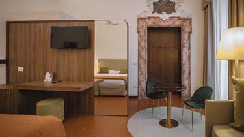 A hotel room with a wooden desk, a television, a bed with a green chair, and a round table with chairs.