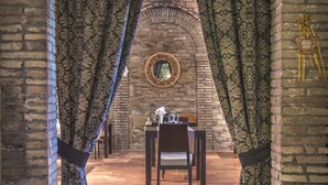 A room with a brick wall, a mirror, a table with chairs, and patterned curtains. - Hotel Villa Montegranelli (Gubbio)