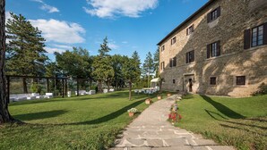 A stone building with a paved courtyard, outdoor seating, and a clear sky. - Hotel Villa Montegranelli (Gubbio)