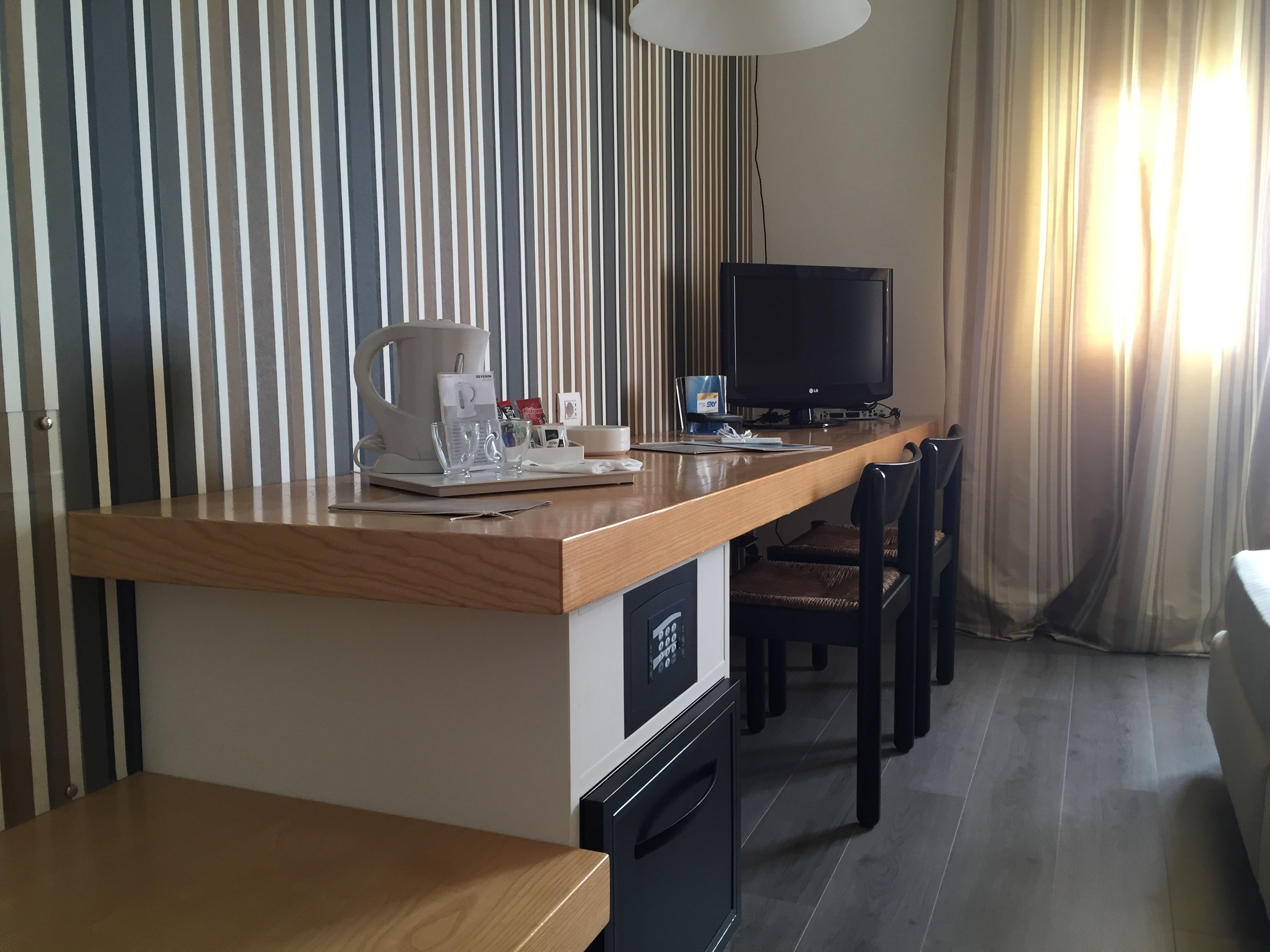 A hotel room with a wooden desk, a television, a coffee maker, and a minibar.