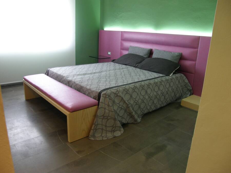 Un dormitorio con cama, banco y paredes verdes.