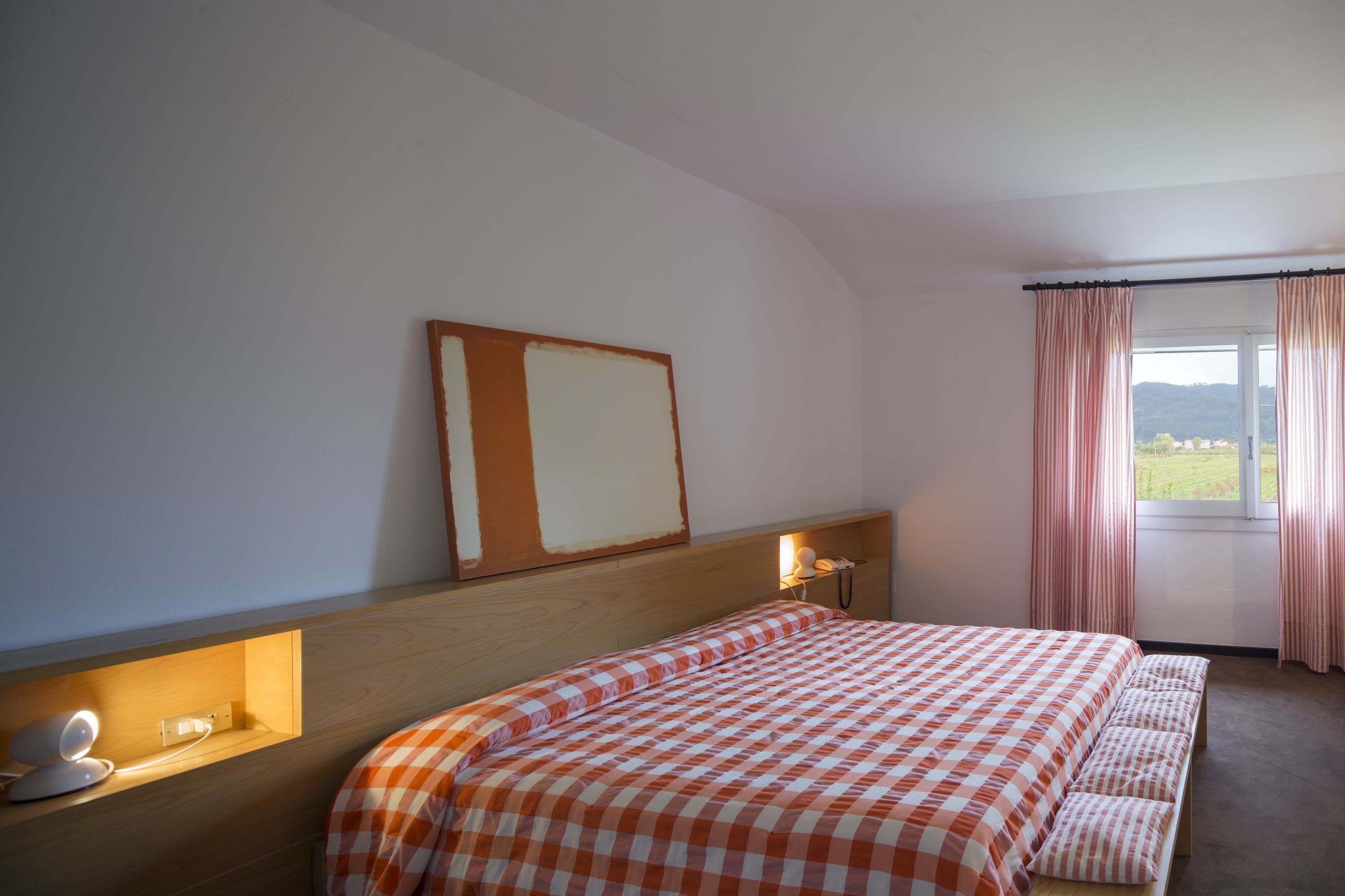 Un dormitorio con cama, mesita de noche, lámpara y ventana con cortinas.