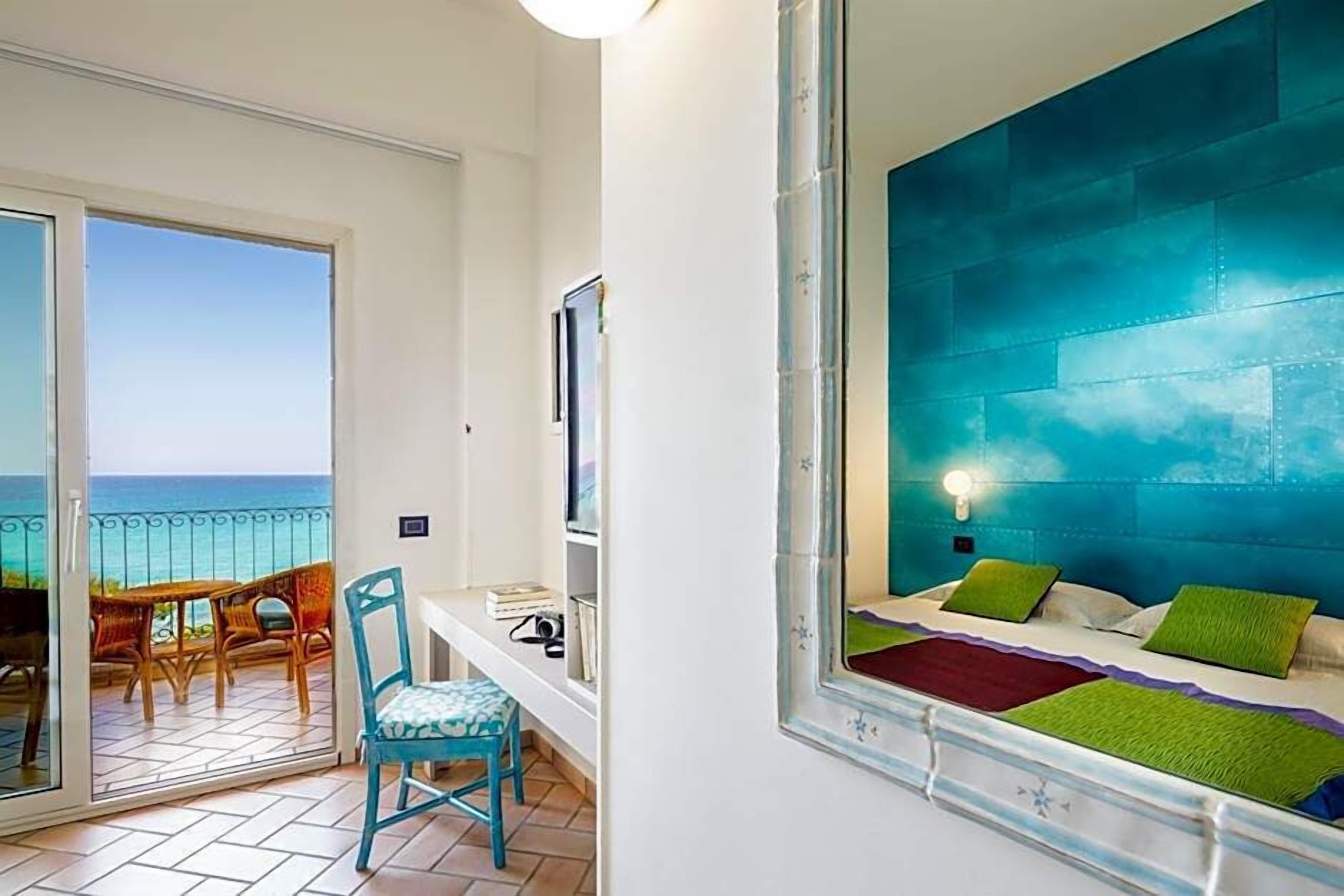 Quarto com cama, poltrona, escrivaninha, televisão e varanda vista para o mar.