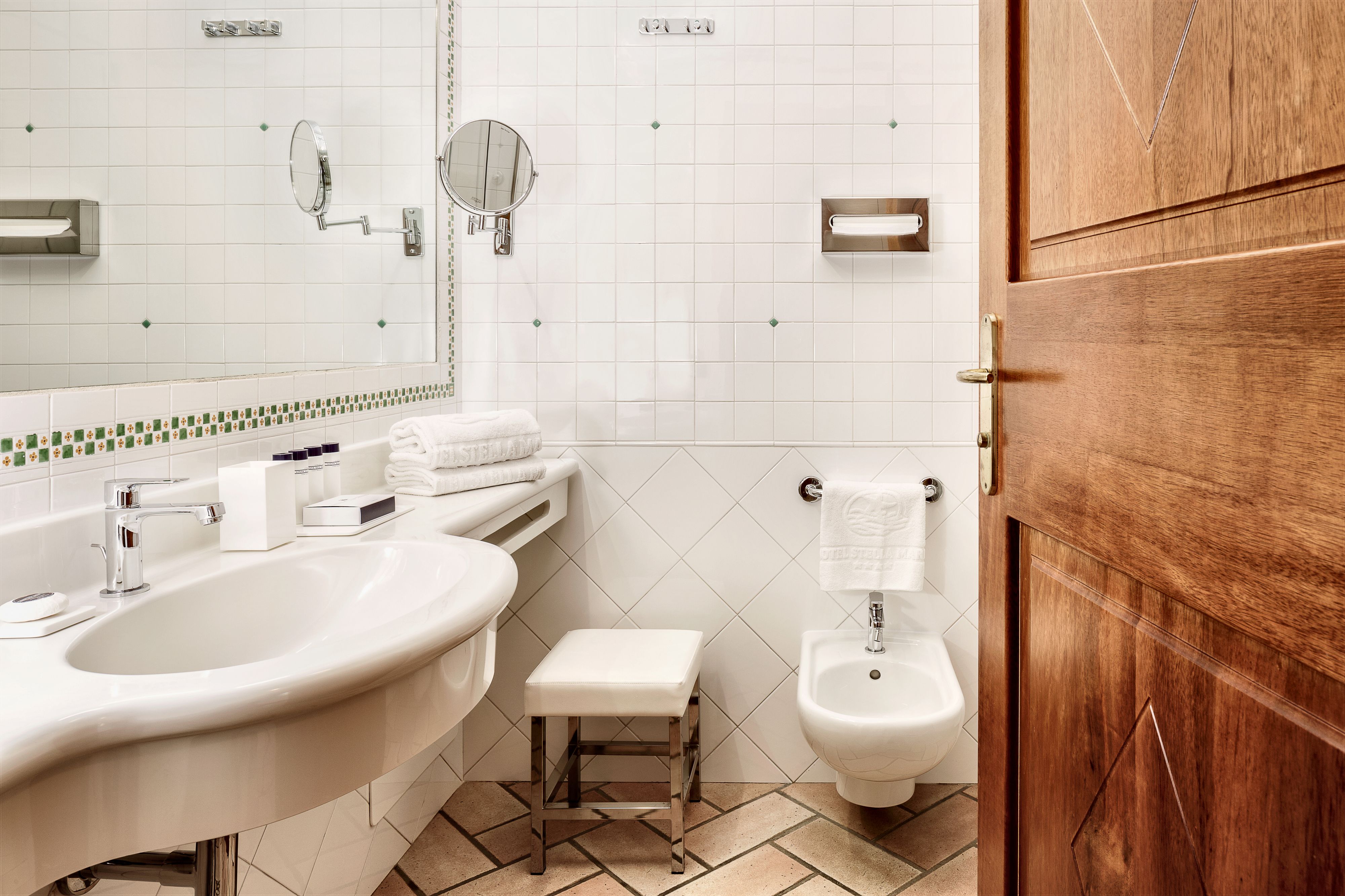 Une salle de bain avec un grand lavabo, deux miroirs, un bidet et une porte en bois.