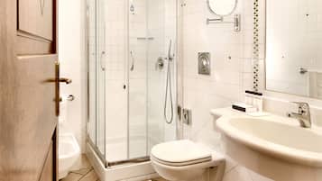 Un baño moderno con ducha de vidrio, inodoro blanco y un lavamanos grande con espejo.
