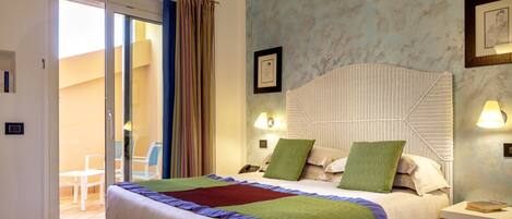Habitación de hotel con cama, mesita de noche, lámpara fijada a la pared y puerta de cristal corredera que da a un espacio exterior con una silla.