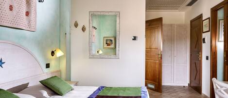 A hotel room with a bed, a nightstand, a wall-mounted lamp, a framed picture, and a wooden door.