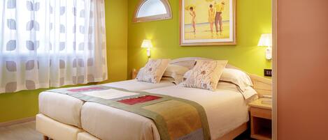 A hotel room with a bed, two bedside tables, a window with curtains, a painting on the wall, and a lamp on each bedside table.