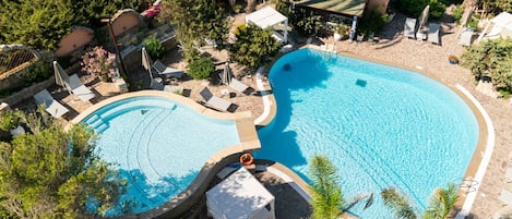 Dos piscinas con sillas de descanso y sombrillas, rodeadas de vegetación y un edificio de piedra.