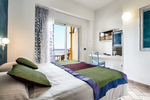 A bedroom with a bed, a chair, a TV, and a door leading to a balcony. - Hotel Stella Maris (Villasimius)