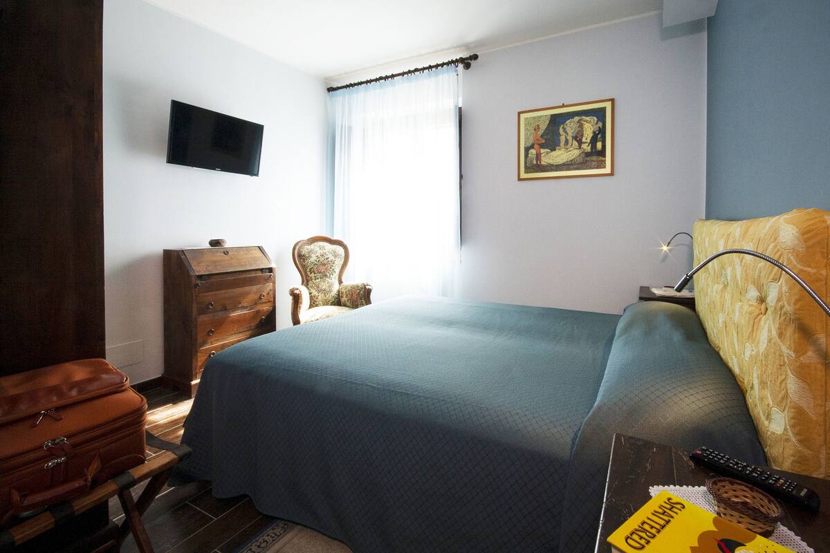 A bedroom with a bed, a dresser, a chair, a television, and a painting on the wall.