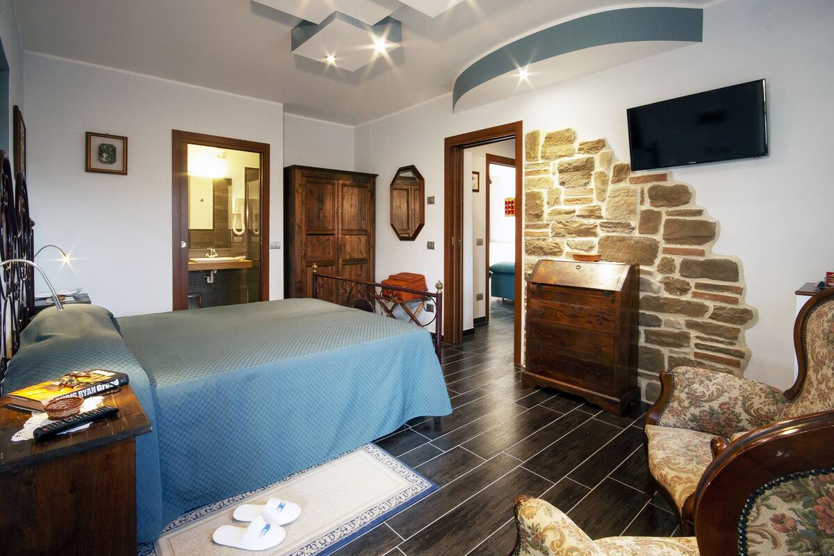 A bedroom with a bed, a dresser, a chair, and a TV on the wall.