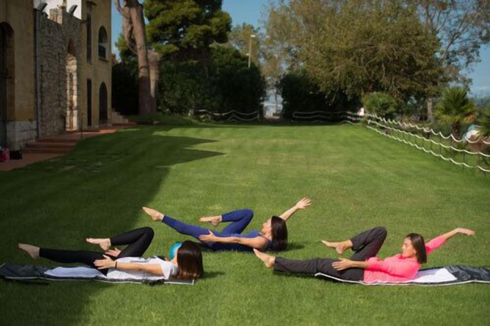 Vier Personen üben Yoga auf einer Wiese, im Hintergrund ein Gebäude.