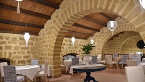 A restaurant with stone walls, wooden beams, and round tables with chairs. - Hotel Tonnara (Trabia)
