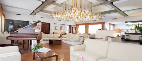 A spacious living area with a grand piano, comfortable seating, and a modern chandelier.