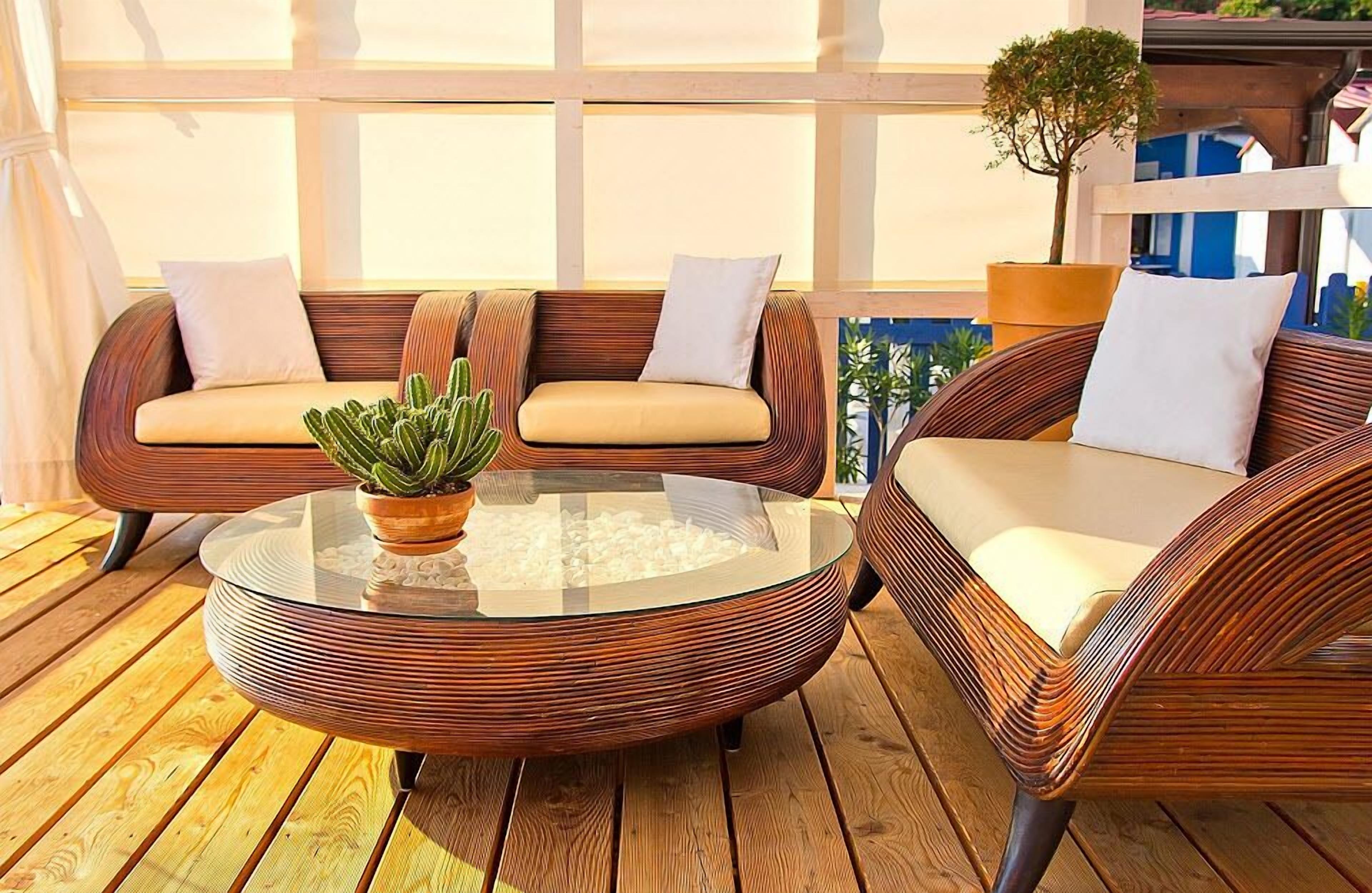 A wooden deck with wicker furniture, including a round glass table and two sofas with cushions.