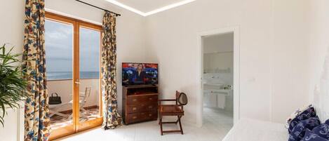 Una habitación con televisión, una silla de madera, una cama y vista al mar a través de un ventanal.