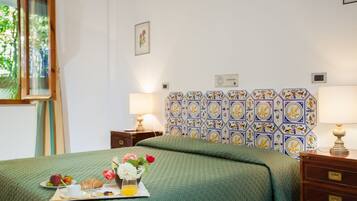Una cama bien tendida con una colcha verde, una bandeja con alimentos para el desayuno y una pared decorada con baldosas hexagonales.